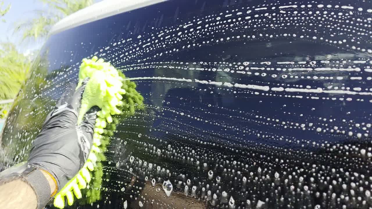 Hand-washing a glossy dark car with a microfiber wash mitt and suds