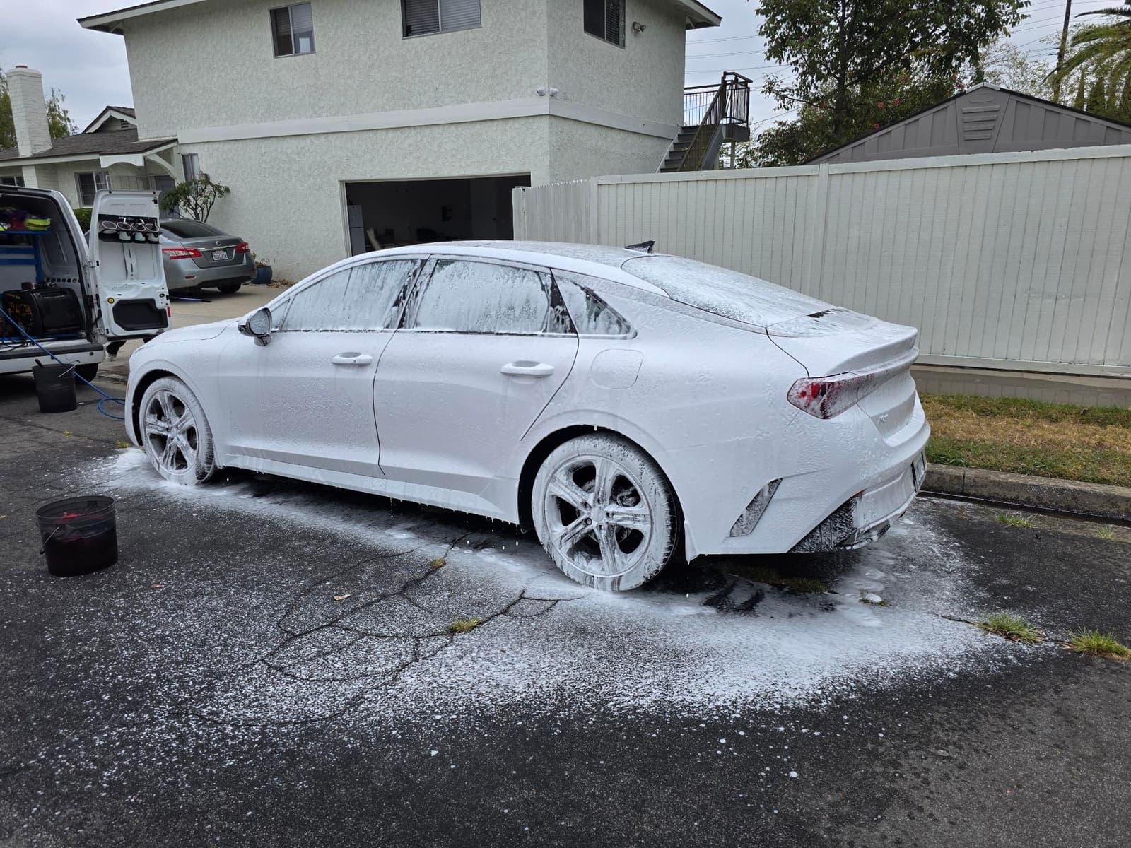 White Kia K5 fully covered in snow foam, rear three-quarter view