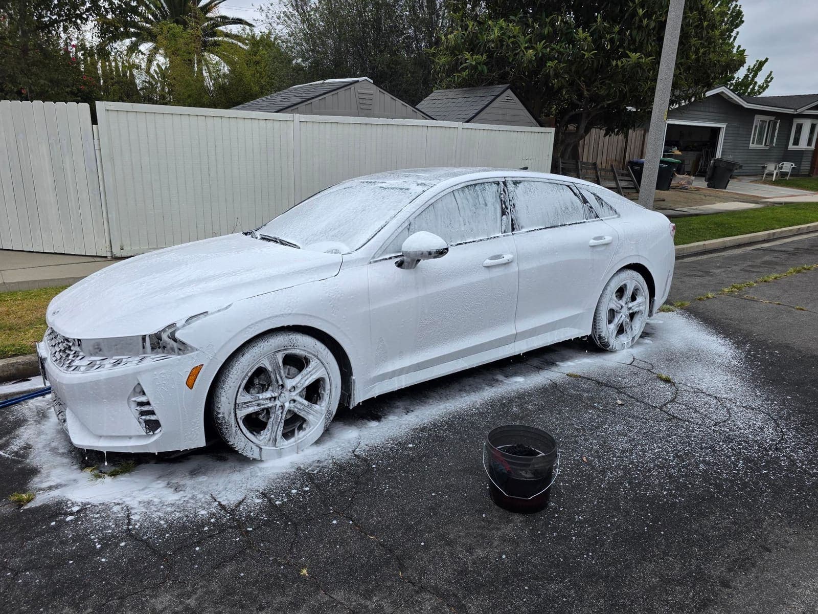 White Kia K5 in full snow foam, front three-quarter view
