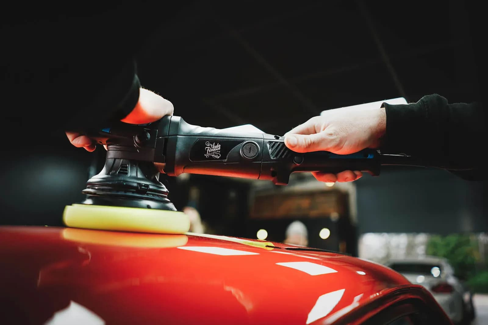 Dual-action polisher with a yellow foam pad working the paint on a red car