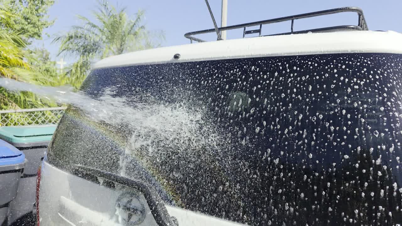 Rinsing suds off the rear glass of a white car in a sunny driveway